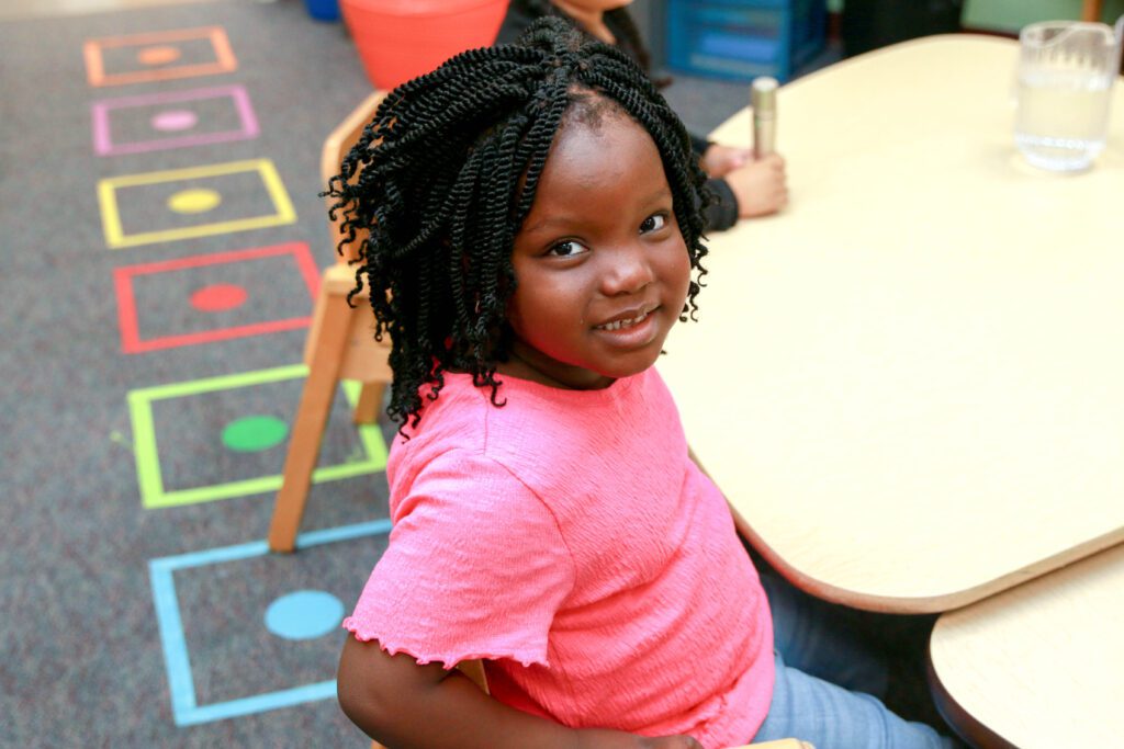 Child smiling at a classroom table.