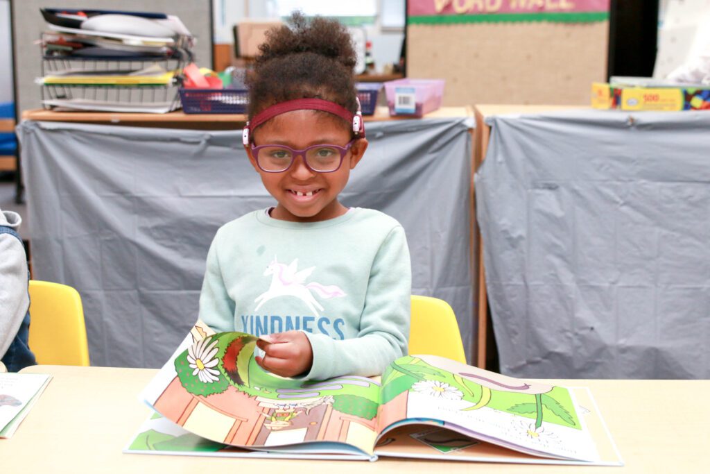 Child smiling while reading a book.